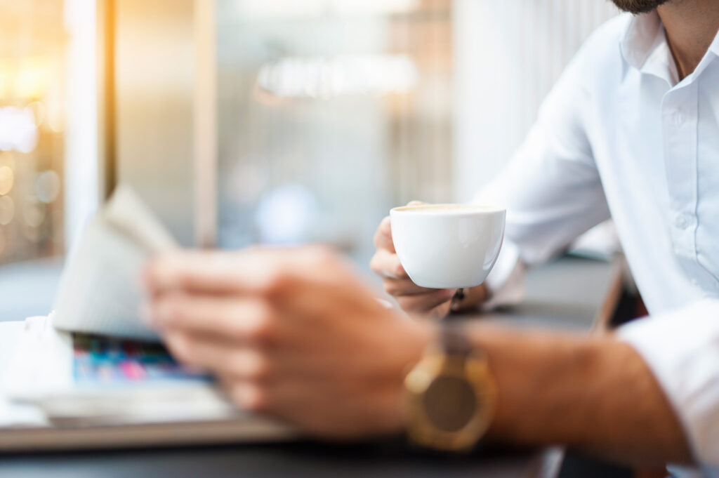 Person liest einen Newsletter und trinkt einen Espresso